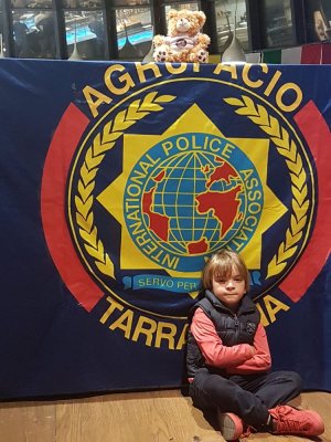 baner z logo IPA Tarragona, na jego tle siedzi dziecko, u góry maskotka turnieju