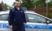 st. sierż. Michał Dudek - Policjant biorący udział w akcji ratowniczej stoi w mundurze na tle oznakowanego radiowozu