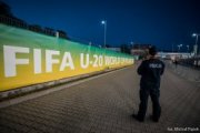 umundurowany policjant stoi przy stadionie piłkarskim obok transparentu z napisem FIFA U-20 World Cup Poland 2019