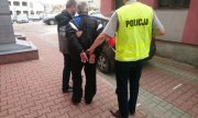 dwaj policjanci prowadzą zatrzymanego mężczyznę do radiowozu