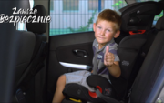 dziecko siedzi w foteliku, w samochodzie i trzyma kciuka do góry. Z lewej strony zdjęcia widnieje napis: zawsze bezpiecznie