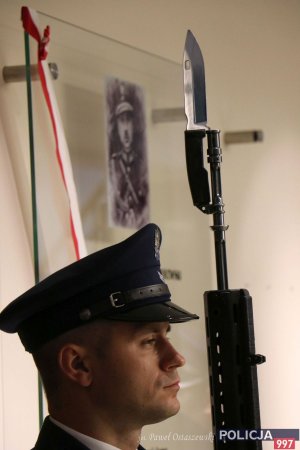Policjant z posterunku honorowego, w tle wizerunek insp. dr. Władysława Sobolewskiego, patrona KGP