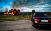 policyjny czarny radiowóz BMW oraz palące się w oddali bele słomy