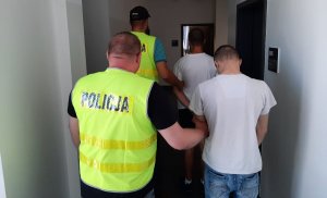 korytarz komisariatu. dwaj policjanci prowadzą zatrzymanych mężczyzn