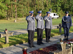 trzej policjanci salutując przed grobami oddają hołd poległym w Palmirach