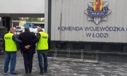 dwaj policjanci konwojują podejrzanego o łapownictwo, zboku logo łódzkiej Policji z napisem Policja, Komenda Wojewódzka w Łodzi