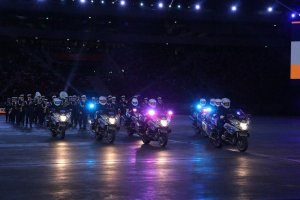 parada: na pierwszym planie policyjne motocykle z włączonymi sygnałami świetlnymi, za nimi maszeruje Orkiestra Reprezentacyjna Policji