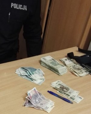 Umundurowany policjant siedzi przy stole a przed nim na tym stole leżą poukładane na kupki pieniądze