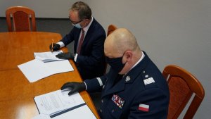 Komendant Wojewódzki podpisuje porozumienie z prezesem Lotosu siedząc przy stole