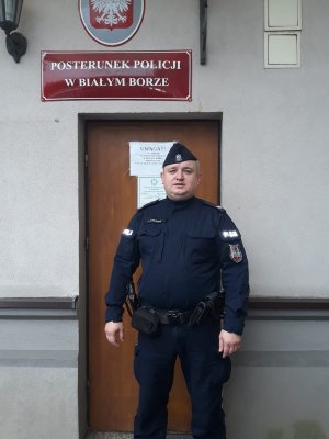 starszy sierżant Przemysław Romańczuk stoi na tle budynku posterunku policji w Białym borze
