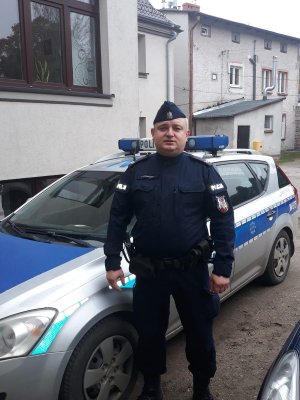 starszy sierżant Przemysław Romańczuk stoi przy radiowozie policyjnym