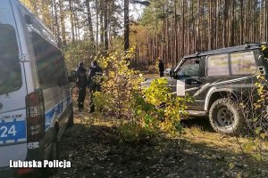 funkcjonariusze podczas poszukiwań w lesie, obok radiowóz i samochód terenowy