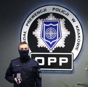 policjant pozuje z medalem w dłoni w tle na ścianie logo Oddziału Prewencji Policji