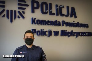 policjant stoi na tle napisu: Komenda Powiatowa Policji w Międzyrzeczu