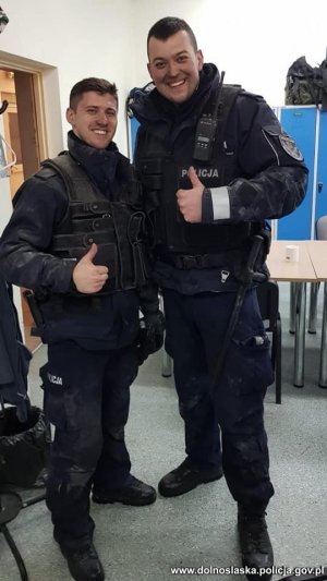 dwaj uśmiechnięci umundurowani policjanci po akcji ratowania kobiety z płonącego mieszkania