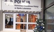 okienko dyżurki Komendy Powiatowej Policji w Opolu Lubelskim. Przed okienkiem widać ustrojoną bombkami i łańcuchami choinkę. na parapecie stoi pociąg