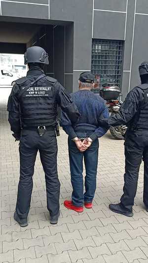 umundurowani policjanci, którzy maj napis: wydział kryminalny na plecach, prowadzą zatrzymanego mężczyznę