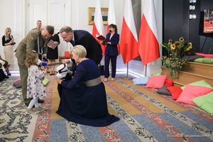 Prezydent Andrzej Duda I pani Prezydentowa Agata Duda pochylają się nad mała dziewczynką, która idzie z mężczyzną w żołnierskim mundurze