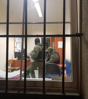 Widok przez okno z kratami na wnętrze pomieszczenia, gdzie znajdują się trzej policjanci
