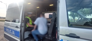w policyjnym furgonie siedzi policjant ruchu drogowego a przed im mężczyzna