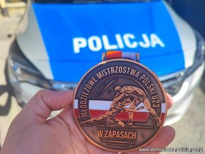 Brązowy medal Młodzieżowych Mistrzostw Polski w Zapasach na tle radiowozu