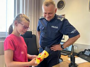 policjant z dziewczynką w pomieszczeniu komendy policji, dziewczynka trzyma lalkę