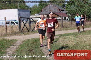 Ubitą drogą, biegnie Arkadiusz Maruszewski, w dalszym planie biegną inni uczestnicy biegu. W prawym dolnym roku, na czerwonym tle jest napis Datasport. Po lewej stronie jest napis: zdjęcie dzięki uprzejmości DataSport.pl