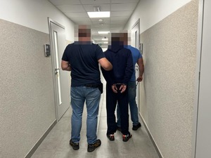dwaj nieumundurowani policjanci prowadzą korytarzem zatrzymanego mężczyznę
