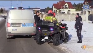 radiowóz policyjny zaparkowany przy drodze obok stoją dwaj policjanci, przy radiowozie stoi quad, na którym siedzą dwaj strażacy biorący udział w poszukiwaniach