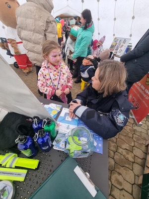 Policjantka przy stoisku profilaktycznym rozmawia z dziećmi.