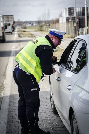 Policjant stoi przy samochodzie i kontroluje kierowcę