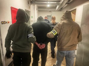 Policjanci ubrani w cywilne ubrania prowadzą zatrzymanego przez korytarz