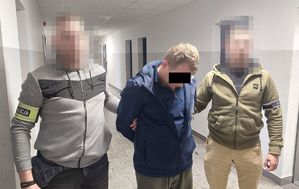 Dwóch policjantów ubranych po cywilnemu prowadzi korytarzem zatrzymanego
