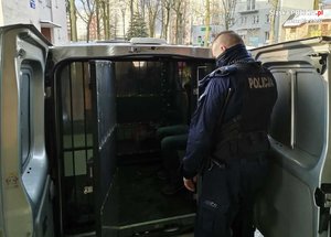 przez otwarte tylne drzwi radiowozu typu bus widać zatrzymanego mężczyznę, przy otwartych drzwiach stoi policjant