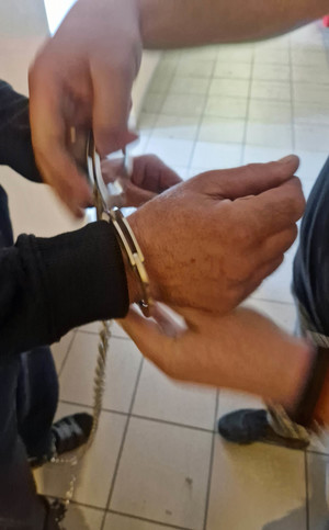 policjant zakłada kajdanki na ręce zatrzymanego