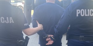 dwaj umundurowani policjanci prowadzą zatrzymanego, który na rękach trzymanych z tyłu ma założone kajdanki