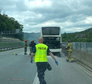 uszkodzony autobus stojący na drodze, obok niego strażacy, w stronę autokaru idzie policjant