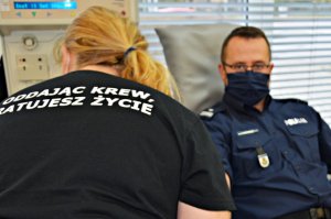 Policjant oddaje krew, na pierwszym planie kobieta w czarnej koszulce z napisem