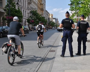 Obok stojącego patrolu policyjnego przejeżdżają rowerzyści.