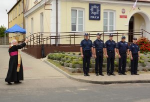 Umundurowani policjanci stojący przed budynkiem posterunku