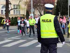 policjant kierujacy ruchem w tle biegnacy maratonczycy