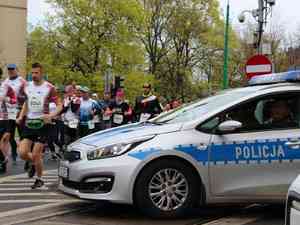 policyjny radiowóz a obok przebiegajacy maratończycy