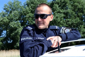 Policjant z Komisariatu Wodnego Policji w mundurze i okularach uśmiecha się opierając o łódkę