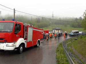 Na zdjęciu z lewej znajduje się wóz strażacki, następnie z oddali widać osoby obserwujące okolice zapory w Wilkowicach, policjantów, strażaków oraz policyjne radiowozy