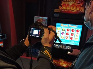 Policjant trzymający w dłoniach aparat fotograficzny i fotografujący automat do gry hazardowej
