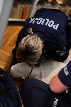 na zdjęciu siedząca na podłodze policjantka, pochylona nad manekinem