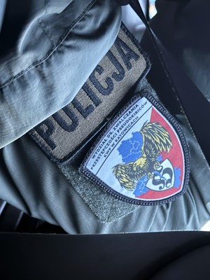 Na zdjęciu fragment ubrania policyjnego, napis Policja i naszywka Wydział Zwalczania Przestępczości Pseudokibiców KWP w Katowicach.