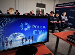 Na pierwszym planie monitor z policyjnym wygaszaczem oraz uczestnicy szkolenia podoficerskiego w tle.