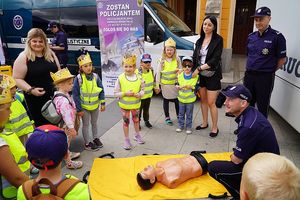 Na zdjęciu dzieci przyglądają się jak policjant instruuje je jak udzielać pierwszej pomocy