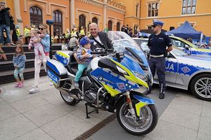 Na zdjęciu chłopczyk siedzący na motorze policyjnym, obok mężczyzna i policjant.